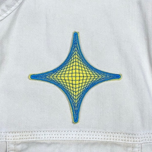 May include: A yellow star-shaped patch with a blue grid pattern, sewn onto a white denim jacket.