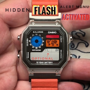 May include: A Casio digital watch with a silver case and an orange band. The watch face displays a world map, a blue dial, and the text "OPTIONAL" and "10 YEAR BATTERY". The word "FLASH" is visible above the watch.