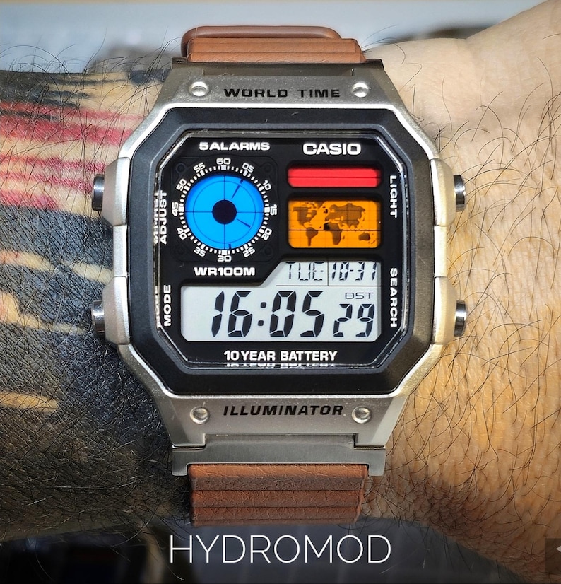 May include: A silver digital watch with a brown leather strap. The watch face displays the time, date, and world map. The watch has the text "WORLD TIME", "CASIO", "10 YEAR BATTERY", and "HYDROMOD".
