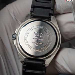 May include: Close-up of a Casio MDV-10 watch back. The stainless steel case features the text "WATER RESISTANT 5 BAR", "JAPAN MOV'T", and "STAINLESS STEEL". The watch has a black rubber strap.