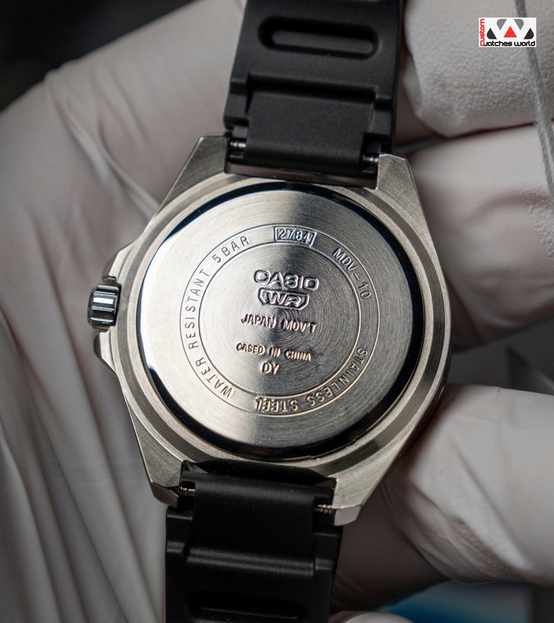 May include: Close-up of a Casio MDV-10 watch back. The stainless steel case features the text "WATER RESISTANT 5 BAR", "JAPAN MOV'T", and "STAINLESS STEEL". The watch has a black rubber strap.