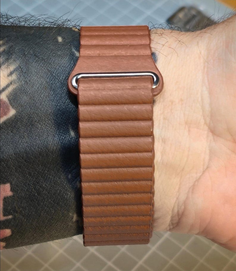 May include: A brown leather watch band with a ribbed design and a silver-colored clasp. The band is shown on a wrist, showcasing its texture and color. The watch band is a stylish accessory.
