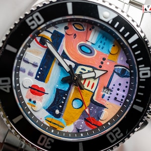May include: A stainless steel wristwatch with a black bezel and a colourful abstract face. The watch face features a vibrant design with orange, blue, yellow, and purple shapes, and black hands. The watch has a date display at the 3 o'clock position.