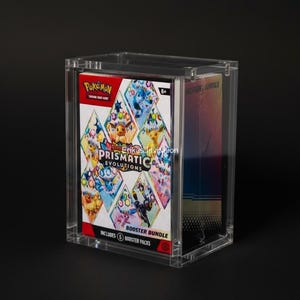 May include: A clear acrylic display case containing a Pokemon Prismatic Evolutions booster bundle. The bundle features colorful artwork of various Pokemon characters. The case also holds additional booster packs, with the text "BOOSTER BUNDLE" visible.