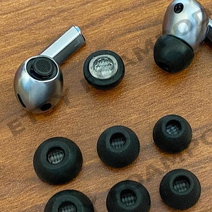 May include: A set of seven black earbud tips for headphones, including one pair of larger tips. The tips are arranged on a wooden surface.  *HEADPHONES NOT INCLUDED*