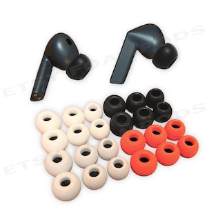 May include: A collection of replacement ear tips in various colors and sizes, including white, black, and orange. Two dark gray wireless earbuds are also present. The ear tips are designed for in-ear headphones.