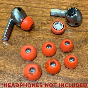 May include: A set of eight orange earbud tips for headphones. The tips are made of a soft, flexible material and come in a variety of sizes to fit different ear shapes.
