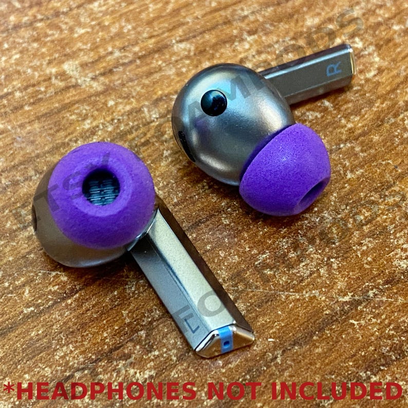 May include: Two purple earbud tips for headphones. The tips are made of soft, flexible material and are designed to fit comfortably in the ear. The tips are shown on a wooden surface.