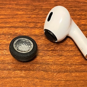 May include: A black earbud tip with a clear plastic mesh insert and a white wireless earbud with a black microphone.