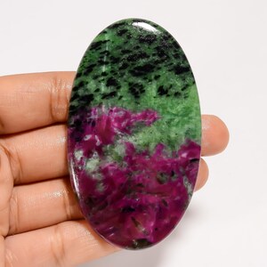 May include: An oval-shaped gemstone with a polished surface. The stone features a striking color combination of green, black, and magenta. The green and black hues are concentrated at the top, while the magenta dominates the lower portion.
