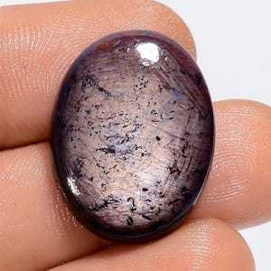 May include: A large, oval-shaped, dark purple gemstone with a silvery sheen and black inclusions. The gemstone is cut and polished.