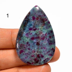 May include: A teardrop-shaped gemstone with a polished surface. The stone features a mix of colors, including deep red, teal, and green. The stone has a speckled appearance, with the red hues concentrated throughout. The number "1" is visible in the upper left corner.