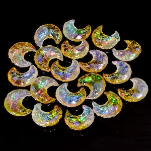 May include: A collection of iridescent glass crescent moon shapes in various shades of yellow, white, and green. The moons are arranged in a circular pattern on a black background.