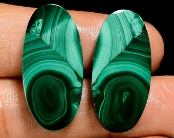 May include: Two oval-shaped malachite gemstones. The gemstones are a deep green color with swirling patterns and a leaf-like design at the top. The stones are polished and smooth, with a high-gloss finish.
