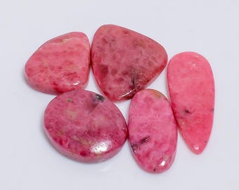 May include: Five polished, pink rhodochrosite gemstones in various shapes. The stones range from oval to irregular, with a mix of light and dark pink hues and subtle veining. The gemstones are displayed on a white surface.