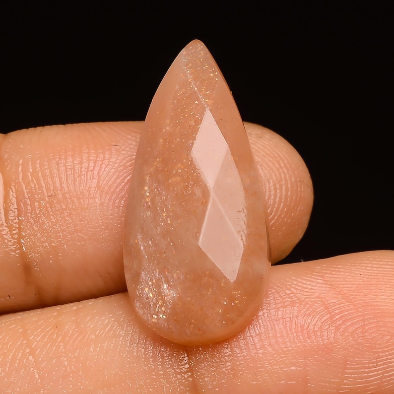May include: A teardrop-shaped sunstone cabochon with a faceted design. The stone is a light orange colour with a shimmery, iridescent finish.