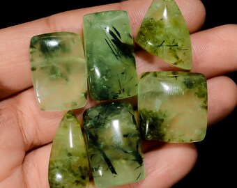 May include: A collection of six green aventurine cabochons with black inclusions. The cabochons are various shapes and sizes, including rectangular, oval, and teardrop.