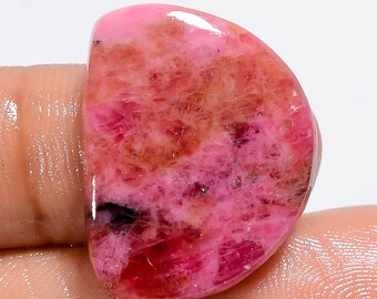 May include: A pink and brown cabochon gemstone with a smooth, polished surface. The stone has a unique, marbled pattern with shades of pink, red, and brown.