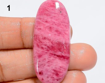 May include: A pink and red oval cabochon gemstone with a swirling pattern. The stone is polished and has a glossy finish.