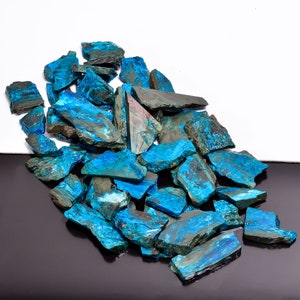 May include: A collection of raw, uncut chrysocolla stones. The stones display a vibrant turquoise and blue color with dark, earthy matrix patterns. The rough-hewn pieces vary in size and shape, creating a natural, organic aesthetic.