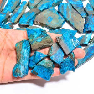 May include: A collection of raw, natural chrysocolla stones. The stones display a vibrant turquoise blue color with areas of brown and gray. The rough, irregular shapes of the stones are visible, showcasing their natural state. The stones are held in a hand.