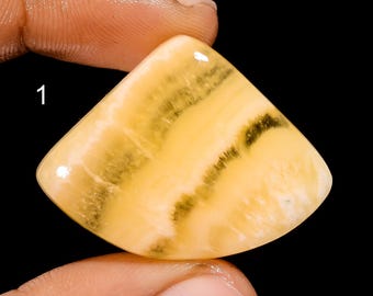 Pode incluir: Um cabochão de ágata amarelo e marrom com uma superfície lisa e polida. A pedra tem aproximadamente 2,5 cm de diâmetro.