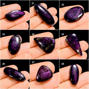 May include: A collection of polished, purple charoite gemstones in various shapes. The stones display a range of dark purple hues with swirling patterns and a glossy finish. Each stone is held in a hand, showcasing the natural beauty and unique characteristics of the gemstones.