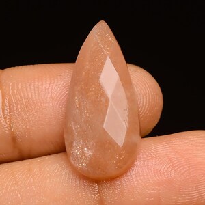 May include: A teardrop-shaped sunstone cabochon with a faceted design. The stone is a light orange colour with a shimmery, iridescent finish.