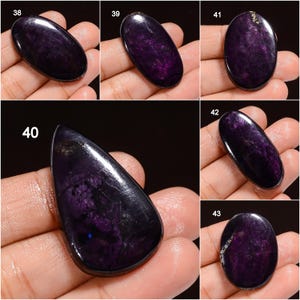 May include: Collection of polished purple sugilite gemstones in various shapes. The stones have a deep, rich color with swirling patterns and a glossy finish. The shapes include oval, teardrop, and rounded forms, showcasing the natural beauty of the material.