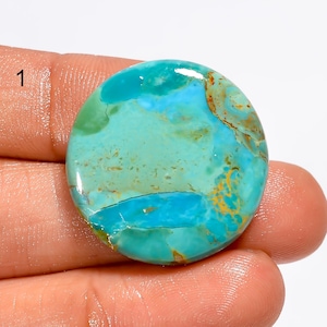 May include: A round, polished turquoise gemstone featuring a vibrant mix of bright sky blue and seafoam green hues, accented by intricate, natural brown matrix veining throughout the surface. The stone is marked with the number 1 in the corner.