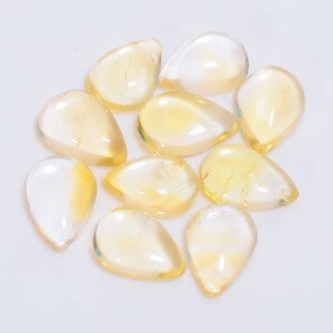 May include: A collection of 10 teardrop-shaped, translucent yellow gemstones. The stones are smooth and polished, with a slight shimmer.