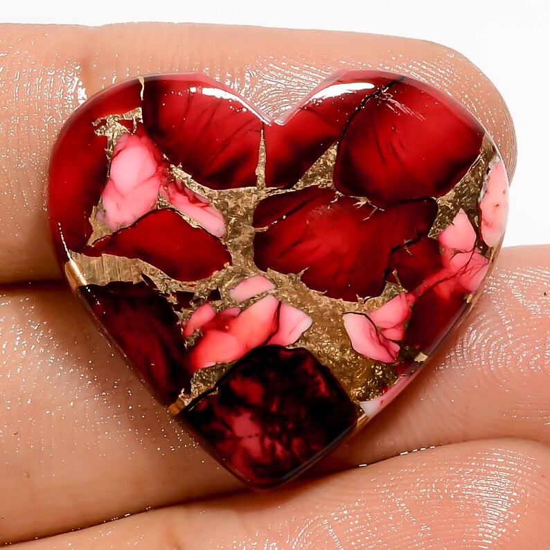 Puede incluir: Una gema en forma de coraz&oacute;n con un vibrante patr&oacute;n rojo y rosa, acentuado por vetas doradas. La superficie pulida refleja la luz, mostrando el intrincado dise&ntilde;o. Esta pieza &uacute;nica es un ejemplo llamativo del arte de las gemas.