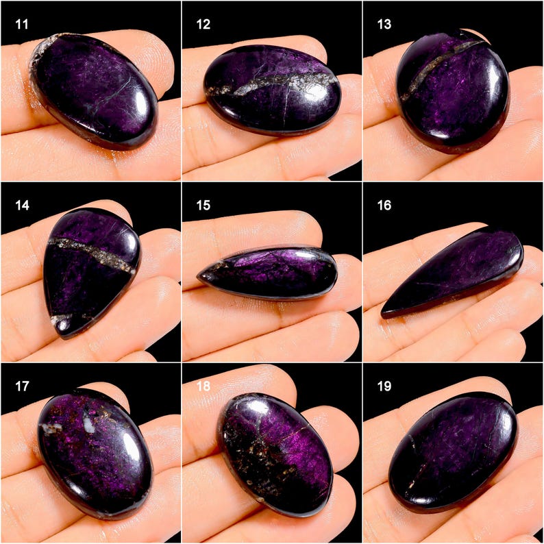 May include: A collection of polished, oval and teardrop-shaped gemstones in varying sizes. The stones are a deep purple color with streaks of silver and white. The gemstones are displayed on a hand, showcasing their smooth, reflective surfaces.