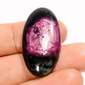May include: An oval-shaped gemstone with a polished surface. The top portion is black, transitioning to a vibrant magenta center with a textured appearance. The bottom section displays a dark green hue.