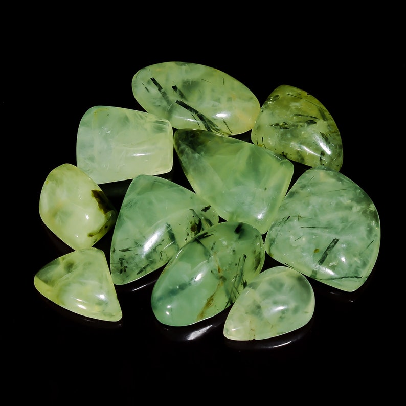 May include: A collection of green aventurine tumbled stones with black inclusions. The stones are smooth and polished, and they have a variety of shapes and sizes.
