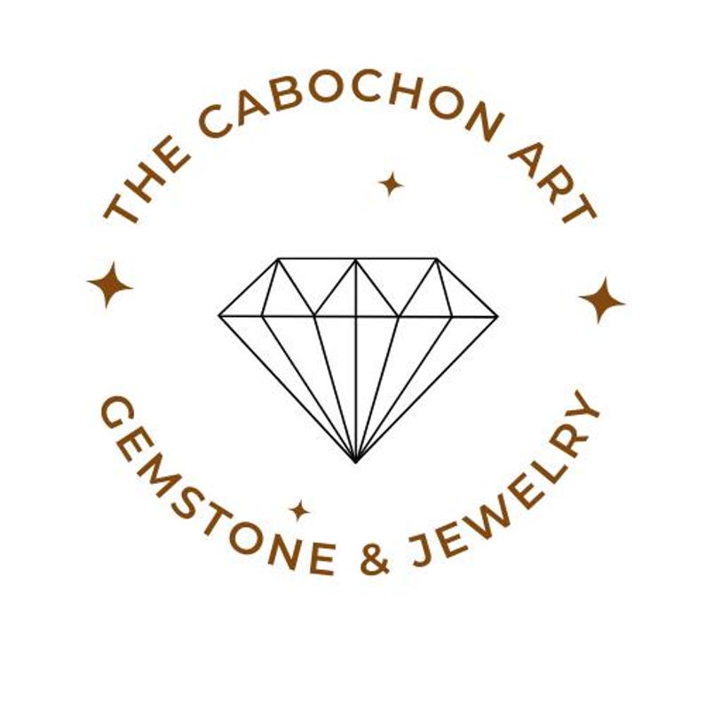 K&ouml;nnte beinhalten: Ein Logo f&uuml;r "The Cabochon Art Gemstone & Jewelry" zeigt eine Diamantenillustration in der Mitte, umgeben von Text in kreisf&ouml;rmiger Anordnung. Text und Diamant sind schwarz und braun auf wei&szlig;em Hintergrund.