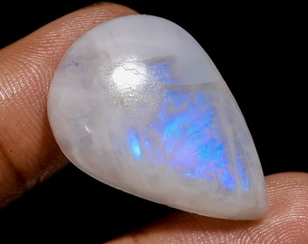 Könnte beinhalten: Ein tropfenförmiger, weißer Mondstein-Cabochon mit schillernden blauen und violetten Blitzen.