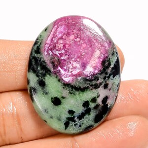 May include: Oval-shaped gemstone with a vibrant pink center and a mix of green and black hues around the edges. The polished surface reflects light, showcasing the natural patterns and textures of the stone. A unique and colorful mineral specimen.