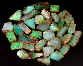 May include: A collection of green and brown chrysoprase gemstones, with a variety of shapes and sizes. The stones are arranged in a circular pattern on a black background.