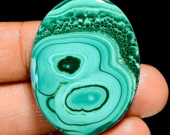 May include: Oval shaped green malachite cabochon with a swirling pattern of light and dark green colors. The stone has a smooth, polished surface.