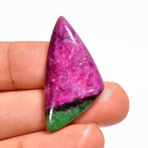 May include: A polished gemstone with a triangular shape. The stone features a vibrant color palette, with a blend of pink, black, and green hues. The pink dominates the upper portion, transitioning to black and then green at the base.