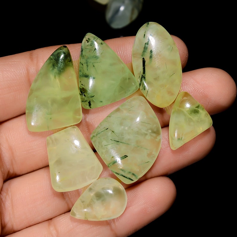 May include: A collection of seven green and yellow gemstone cabochons with a variety of shapes and sizes. The stones have a translucent appearance with visible inclusions.