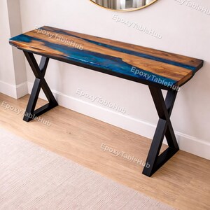 May include: A wooden console table with a blue epoxy resin river design. The tabletop is supported by black metal X-shaped legs. The table is approximately 60 inches long.