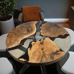 Pode incluir: Uma mesa redonda de madeira com um design único. A mesa apresenta um padrão de grão de madeira castanho claro com um rio de resina epóxi cinza escuro. A mesa é suportada por pernas de metal e é rodeada por cadeiras cinzentas.