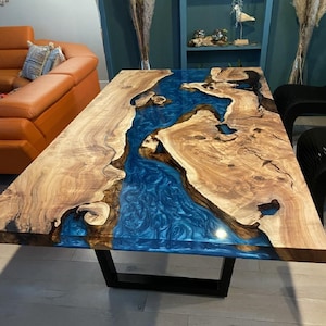 Puede incluir: Una gran mesa de comedor de madera con un río de resina epoxi azul que atraviesa el centro. La mesa tiene una base de metal negro.
