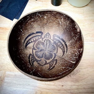 Pode incluir: Uma tigela de coco marrom com um desenho preto e branco de uma tartaruga com uma flor de hibisco nas costas.