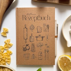 Könnte beinhalten: Ein Kochbuch aus Kraftpapier mit dem Titel "Bettinas Rezeptbuch" mit Illustrationen von Küchenutensilien und Zutaten. Das Bild zeigt frische Tomaten, Pasta, Zitronen, Basilikum und einen Holzlöffel.