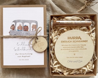 Könnte beinhalten: Ein Geschenkset für den ersten Schultag eines Kindes. Das Set enthält eine Karte mit einer Busillustration und Text sowie ein Holzschild mit der Aufschrift "1. Klasse!". Die andere Box enthält eine Holzscheibe mit Text und ein Glasröhrchen.