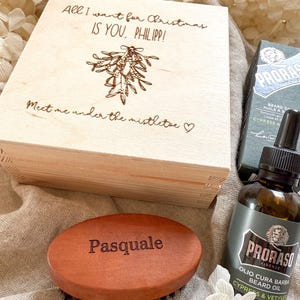 Könnte beinhalten: Holzgeschenkbox mit dem Text "All I want for Christmas is you, Philipp!" und "Meet me under the mistletoe". Enthält eine Bartbürste mit dem Namen "Pasquale" und Bartöl.