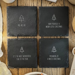 Könnte beinhalten: Vier quadratische schwarze Schieferuntersetzer mit weißem Text und einem Weihnachtsbaumdesign. Die Untersetzer tragen die Aufschriften "Ho, Ho, Ho", "Have yourself a Merry Little Christmas", "It's the most wonderful time of the year" und "Dreaming of a white Christmas".